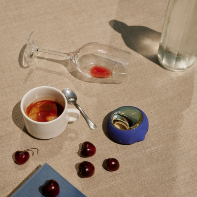 Mesa bege com copo tombado, xícara de café, cerejas, colher, cinzeiro azul e garrafa.