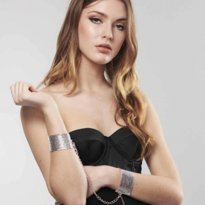 Mulher com vestido preto e pulseiras prateadas largas com corrente