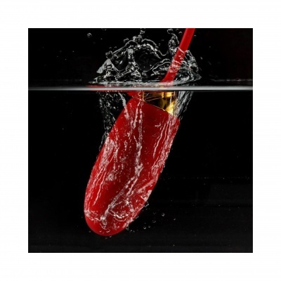 Produto vermelho e dourado submerso em água com respingos, fundo preto