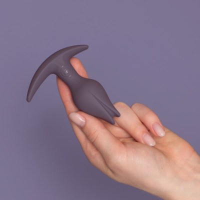 Plug anal cinza escuro segurado por mão feminina com fundo roxo