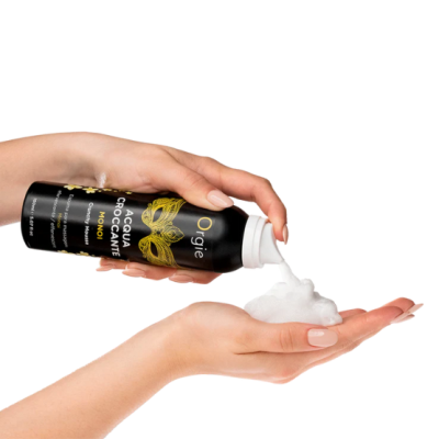 Espuma de beleza num frasco preto com texto dourado e branco a ser aplicada nas mãos.