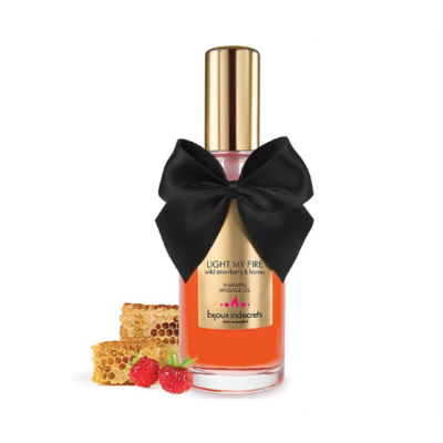 Frasco de óleo de massagem com tampa dourada e laço preto, junto a favo de mel e morangos silvestres