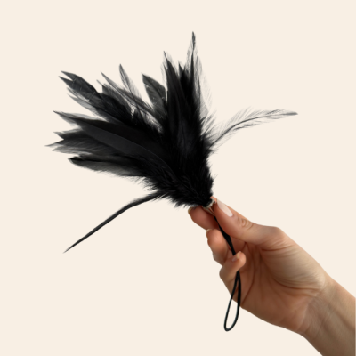 Catavento de penas pretas segurado por uma mão sobre fundo bege claro