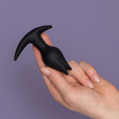 Mão segurando dispositivo preto de silicone com asa em T e texto STROKER.