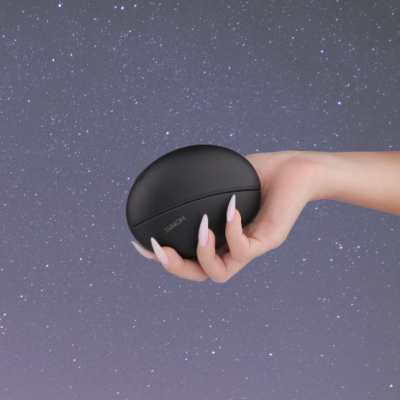 Mão a segurar uma caixa preta ovalada com o nome Samsung contra fundo estrelado