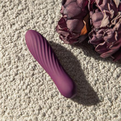 Vibrador roxo com textura ondulada e flores secas ao lado