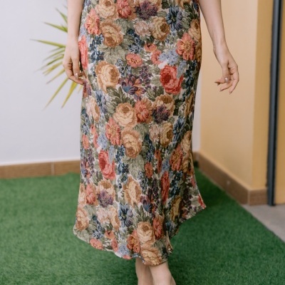 Saia midi floral colorida usada com camisola branca e sandálias trançadas, em ambiente externo com relva artificial.
