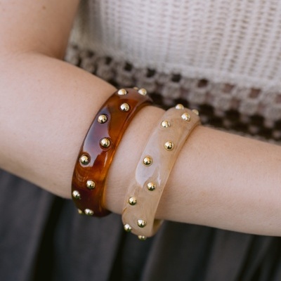 Braceletes castanha e bege com tachas douradas num braço