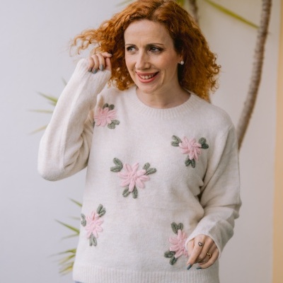 Mulher a usar camisola branca com flores rosas bordadas e calças de ganga azuis, com planta ao fundo