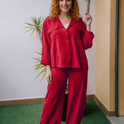 Mulher com camisa vermelha e calças largas vermelhas e botas douradas em ambiente com relva e plantas