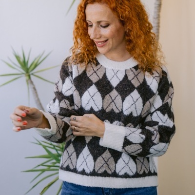 Mulher com camisola de losangos e jeans junto a plantas em ambiente interior