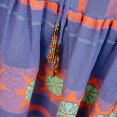 Tecido azul com padrões geométricos laranja e verde e detalhes com contas