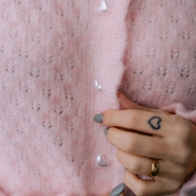 Casaco rosa claro com botões em forma de coração e detalhe nas mãos a abotoar