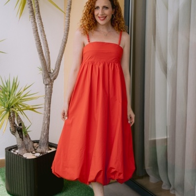 Mulher com vestido vermelho e sandálias camel perto de planta em vaso preto