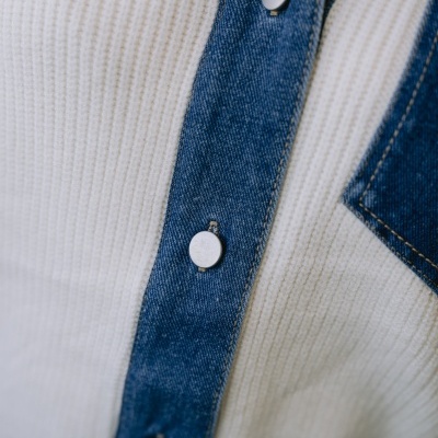 Close-up de tecido branco com faixa azul em ganga e botões metálicos prateados