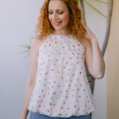 Blusa branca de bolinhas coloridas usada por mulher com cabelo ruivo