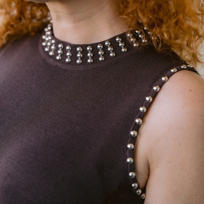 Top castanho de malha com tachas metálicas na gola alta e nas mangas, usado por pessoa ruiva.