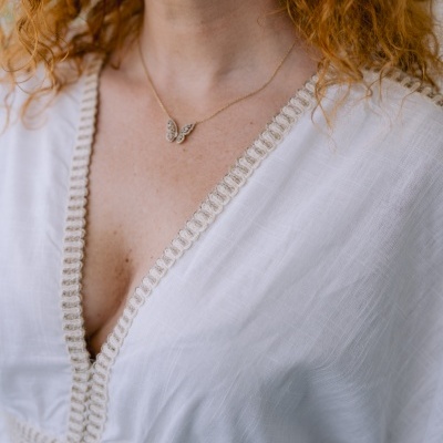 Colar borboleta dourado no pescoço de mulher com blusa branca rendada.