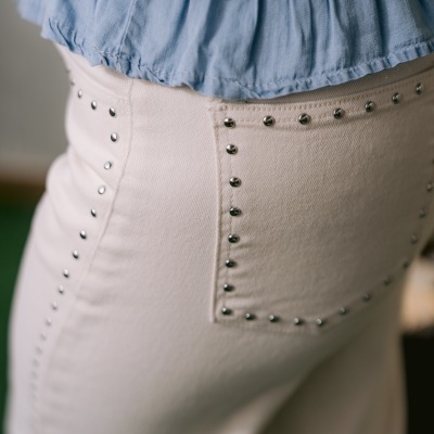 Calças bege com rebites metálicos e blusa azul clara com cintura franzida