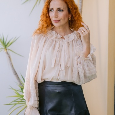 Mulher vestindo blusa bege leve com gola e punhos franzidos e saia preta de pele sintética.