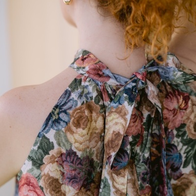 Mulher de costas com vestido floral colorido e laço no pescoço.