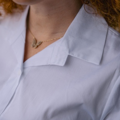 Colar dourado com borboleta usado por pessoa com camisa branca e cabelo ruivo encaracolado.