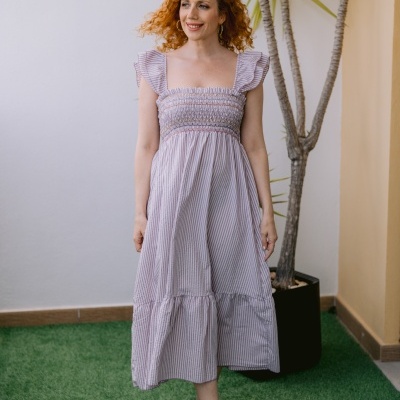 Mulher com vestido riscado cor-de-rosa claro em ambiente com relva sintética e planta