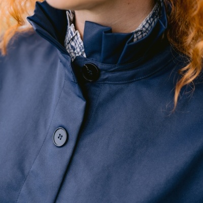 Casaco azul escuro com botões e gola alta, detalhe de camisa xadrez e brinco dourado em cabelo ruivo.