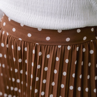 Saia plissada castanha às bolas brancas com blusa branca enrugada.