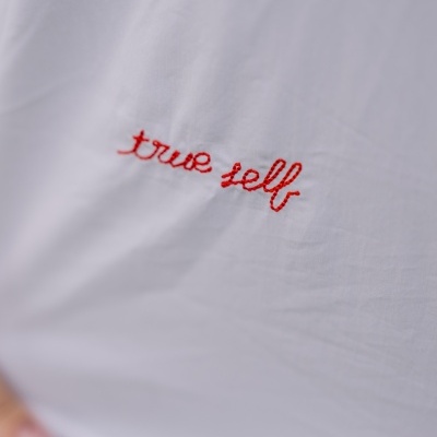 Peça de roupa branca com bordado vermelho com as palavras true self.