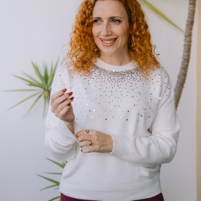 Mulher com camisola branca com lantejoulas e saia vinho em fundo branco com plantas.