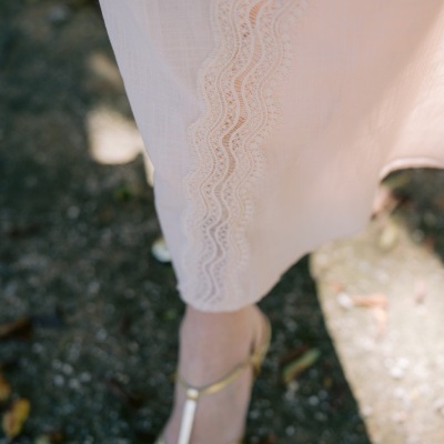 Saia comprida creme com renda ondulada e sandálias douradas em chão de pedra