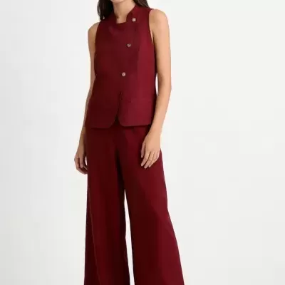 Conjunto feminino vermelho vinho com colete e calças largas e sandálias brancas.