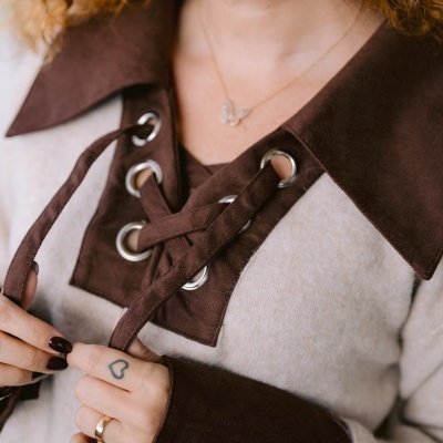 Pullover cinzento com detalhes castanhos e cordão largo em ilhóses metálicos, usado por pessoa com cabelo ruivo