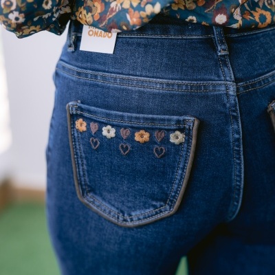 Jeans azuis com bolso bordado com flores e corações e etiqueta branca com texto em laranja