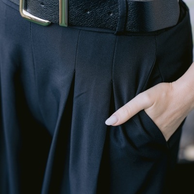 Cinto preto de couro com fivela prateada e calças pretas com pregas.