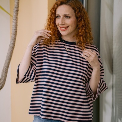 Mulher com camisola de riscas rosa e azul posando junto a uma janela