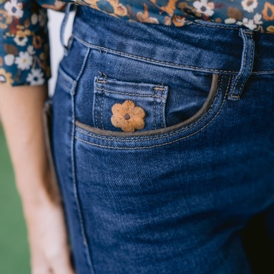 Calças de ganga azul escura com bordado de flor castanha no bolso traseiro e camisa floral azul com padrão multicolorido.
