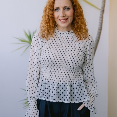 Blusa branca com bolinhas pretas e mangas longas num ambiente interior com planta ao fundo