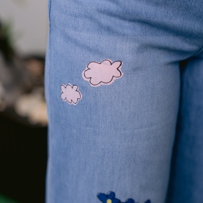 Calças de ganga azul claro com estampas de nuvens cor de rosa e flores azuis.