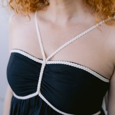 Vestido preto com tiras trançadas bege no decote e alças cruzadas.