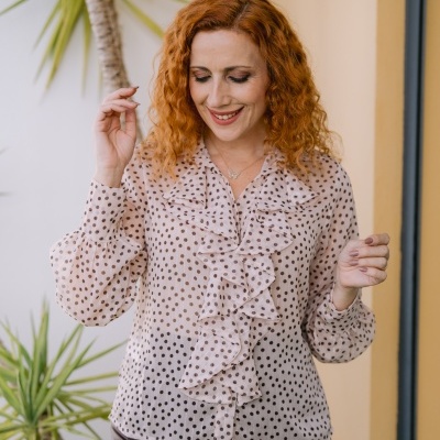 Blusa bege com bolinhas castanhas e folhos usada por mulher com calças de couro castanhas