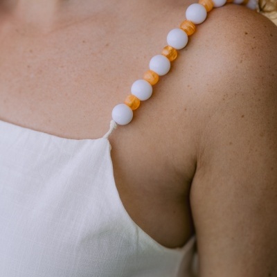 Vestido branco com alças de contas brancas e laranja em ombro de mulher