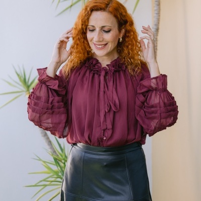 Mulher com blusa vinho de mangas bufantes e saia preta midi em ambiente exterior com plantas