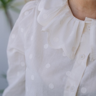 Blusa branca com padrões de bolinhas em relevo e gola com abas em forma de pétalas