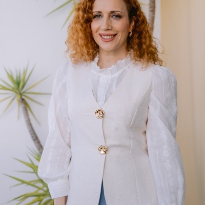 Mulher de cabelo ruivo com colete branco e camisa branca com mangas bufantes com saia azul