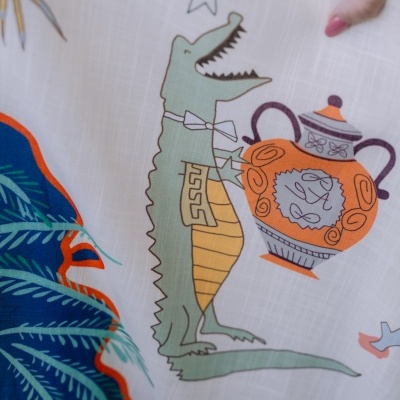 Pano branco com estampado de crocodilo, jarro e elementos decorativos coloridos