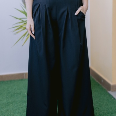 Calças pretas largas com cinto preto e camisa branca em ambiente com relvado e planta