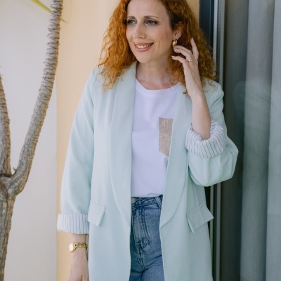 Mulher com blazer verde-água e t-shirt branca junto a parede bege