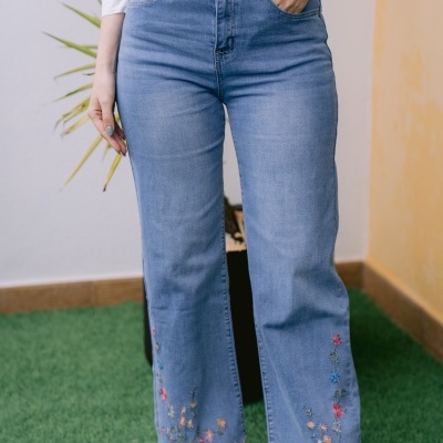 Calças de ganga azul com bordados florais e camisa branca com estampado de vasos de flores.